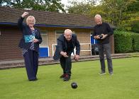 Councillor Matt Swindlehurst (centre) tries his hand at bowls on the green at Brough Park watched by Staffordshire Moorlands District Chairman, Councillor Lyn Swindlehurst, and Neil.